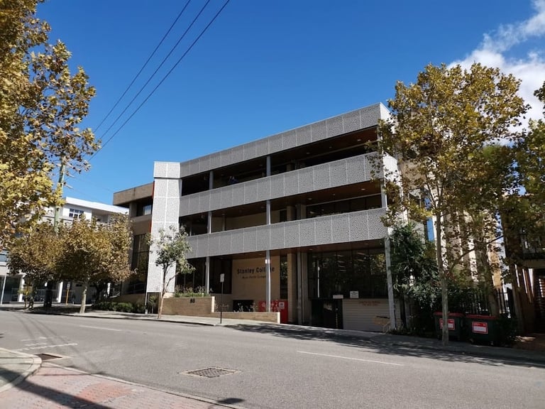 Modern concrete building with multiple stories and large windows on a sunny street with trees and utility lines