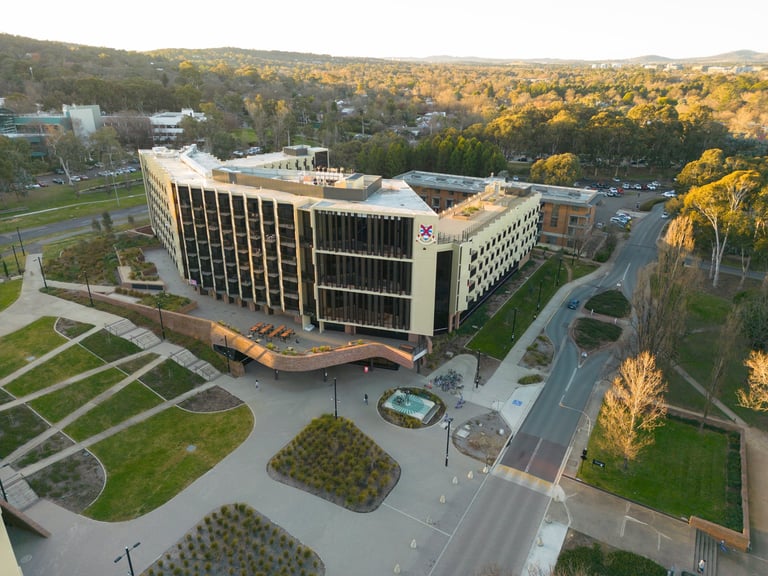 Aerial view of a modern multi-story institutional building with geometric architecture surrounded by landscaped grounds and forested area