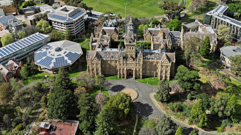 Aerial view of a large Gothic stone castle surrounded by green grounds and modern buildings on a university campus